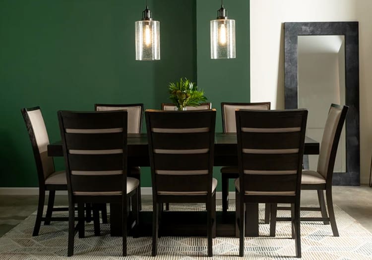 Dark wood dining table set with six cushioned chairs, beige upholstery, green accent wall, pendant lights, and large floor mirror.