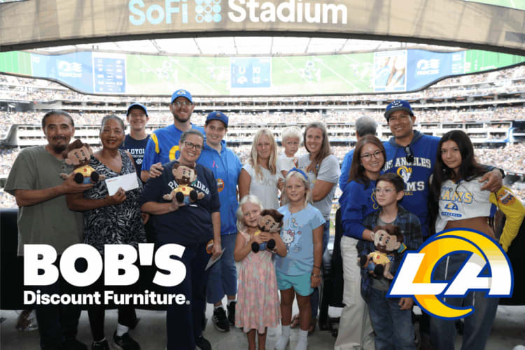 Group of people at SoFi Stadium holding plush toys, wearing Los Angeles Rams apparel, with logos for "BOB'S Discount Furniture" and "LCA" visible.