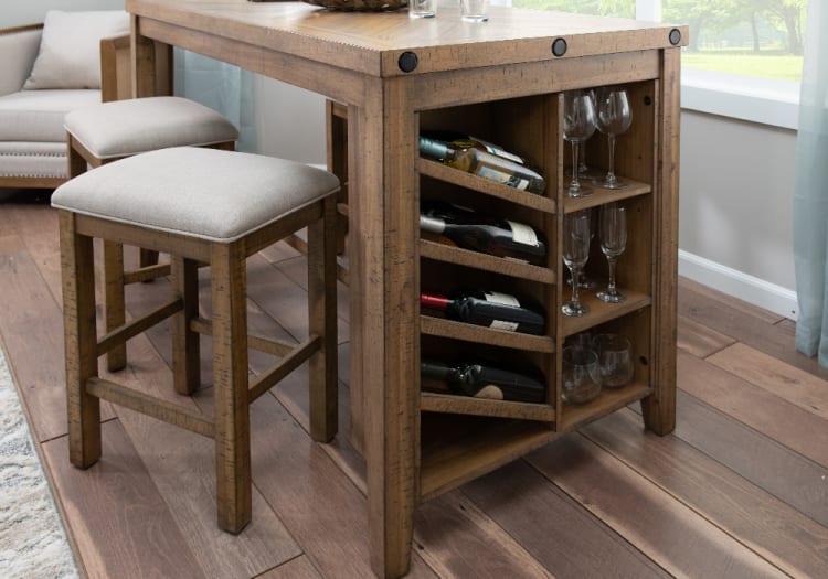 Rustic wooden kitchen island with built-in wine rack holding four bottles and adjacent shelves storing various wine glasses, paired with two cushioned beige bar stools on hardwood flooring.