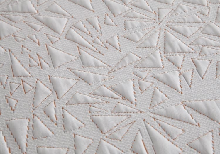 White quilted fabric with a geometric pattern of stitched triangles, showcasing detailed texture and modern design.