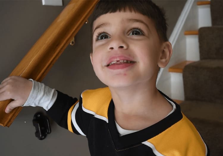Child wearing a black and yellow sports jersey with white accents, standing near a wooden handrail by carpeted stairs.