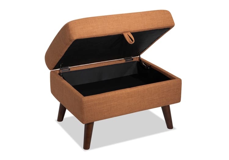 Mid-century modern storage ottoman in brown fabric with wooden tapered legs, featuring a hinged top for hidden storage space.
