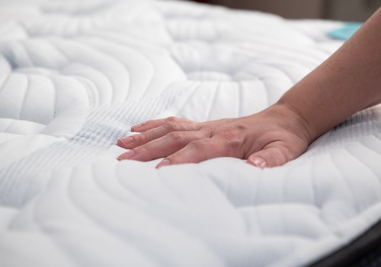 Hand pressing down on a white, quilted mattress with textured stitching, demonstrating mattress softness and comfort.