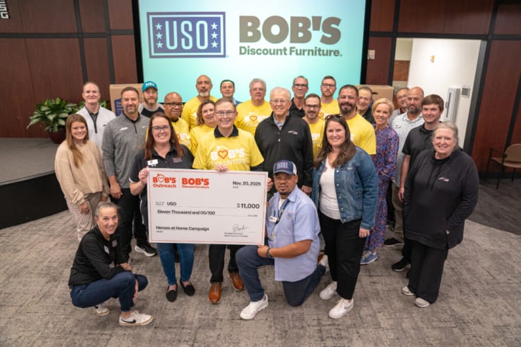 Group of volunteers holding a large $11,000 check from Bob's Discount Furniture for the USO Heroes at Home Campaign, dated Nov 20, 2025.