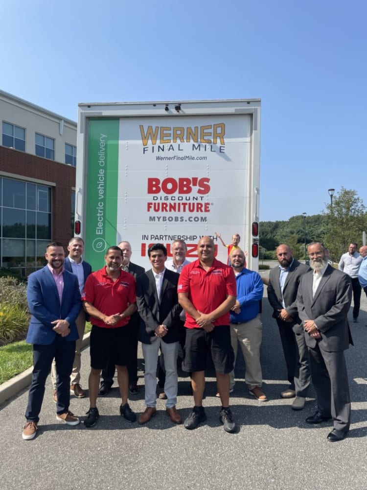 Group of men standing in front of a Werner Final Mile delivery truck featuring Bob's Discount Furniture branding and partnership with Isuzu, outdoors on a sunny day.