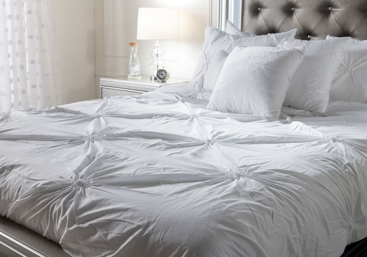 White tufted comforter set on a bed with matching decorative pillows, featuring a soft, textured fabric and a modern, elegant bedroom setting.