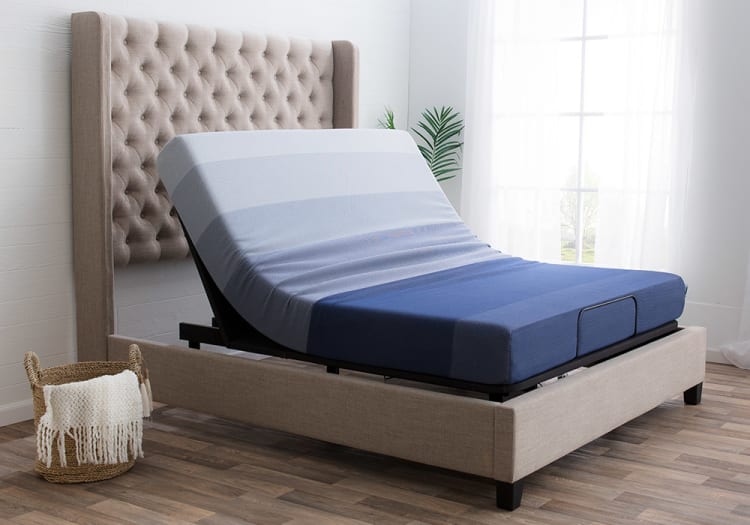 Adjustable bed with a tufted beige fabric headboard and a blue gradient memory foam mattress, set in a modern bedroom with wood flooring.