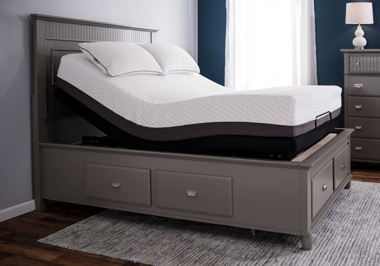 Adjustable gray wooden bed frame with white textured mattress and two pillows, featuring a raised head section for ergonomic comfort.