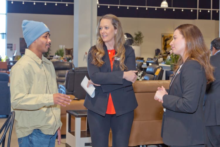 Three people engaged in conversation inside a modern furniture showroom, featuring leather sofas and contemporary decor in the background.