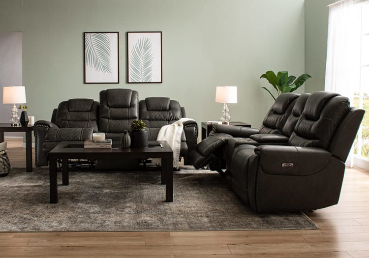 Contemporary living room with dark gray leather reclining sofas, a black wooden coffee table, side tables with glass lamps, green plant, and framed leaf artwork.