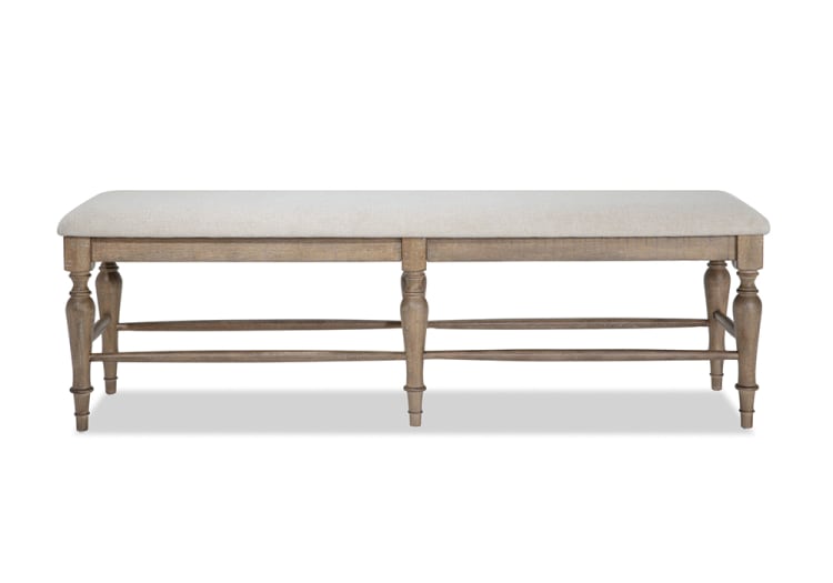 Upholstered beige fabric bench with a wooden frame and turned legs, featuring a rustic, natural wood finish, suitable for dining or entryway seating.