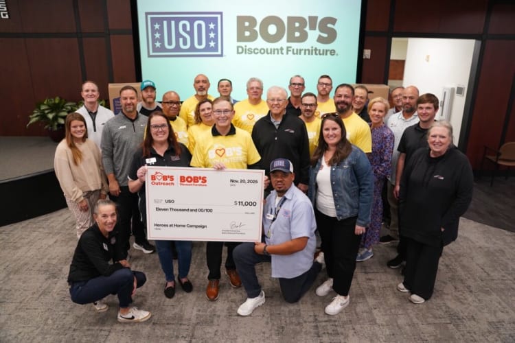 Group of people holding a large check for $11,000 donation from Bob’s Discount Furniture to USO Heroes at Home Campaign, with USO and Bob’s logos in the background.