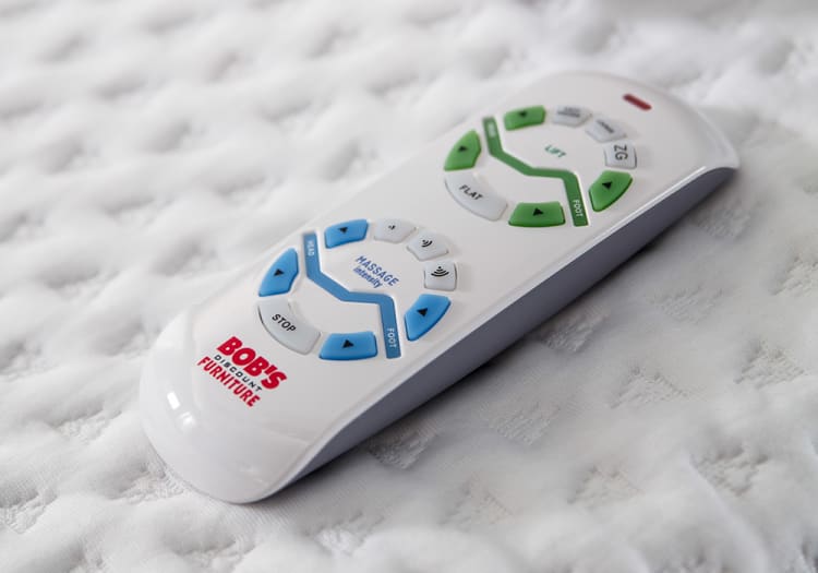 White remote control for adjustable furniture from Bob's Discount Furniture, featuring blue and green buttons for massage intensity, head, foot, lift, and flat settings.