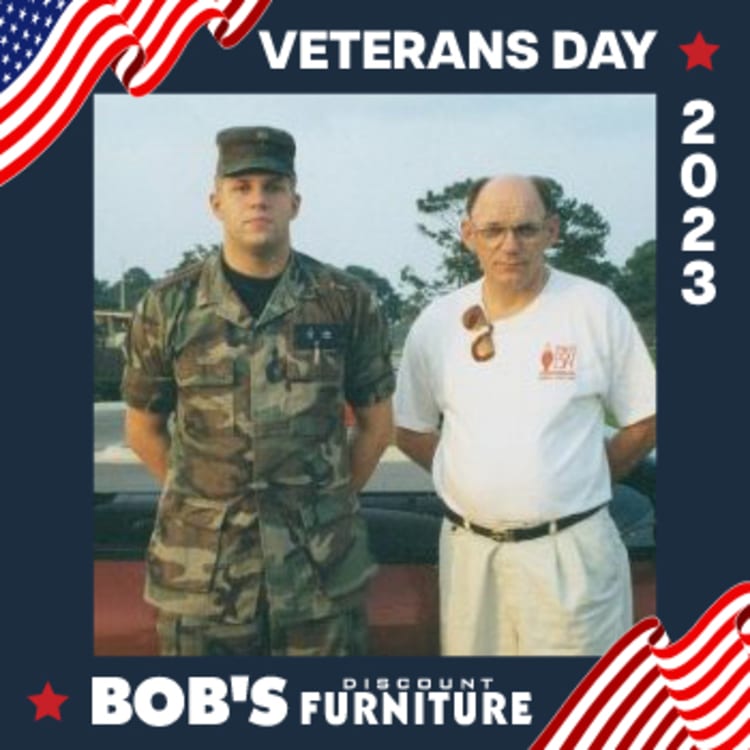 Two men standing side by side, one in camouflage military uniform and the other in white polo and khaki pants, framed by a Veterans Day 2023 graphic with red, white, and blue patriotic accents and "Bob's Discount Furniture" branding.