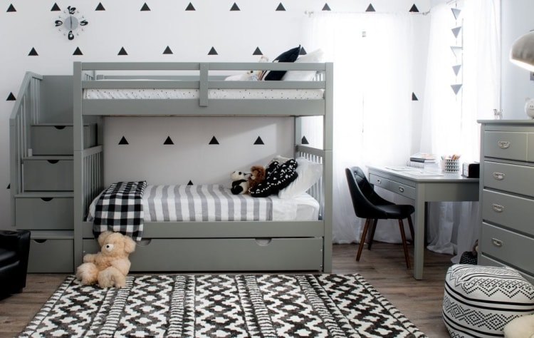 Gray wooden bunk bed with stairs, black and white striped bedding, stuffed animals, a patterned rug, gray desk with black chair, and matching dresser in a modern kids' bedroom.