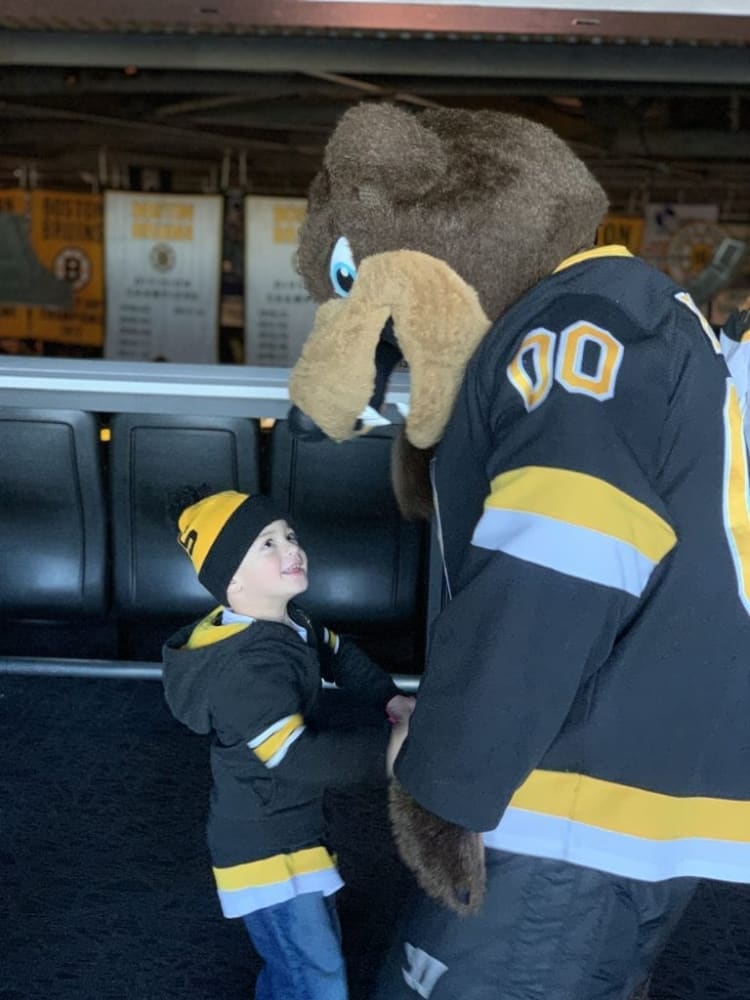 Child wearing a black and yellow Boston Bruins hoodie and matching beanie interacting with the Bruins mascot in a black and yellow jersey.