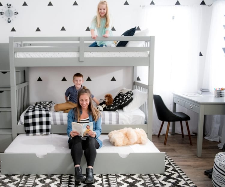 Children's bedroom with gray wooden bunk bed, black and white checkered blanket, striped bedding, plush toys, and a gray desk with black chair by a window.