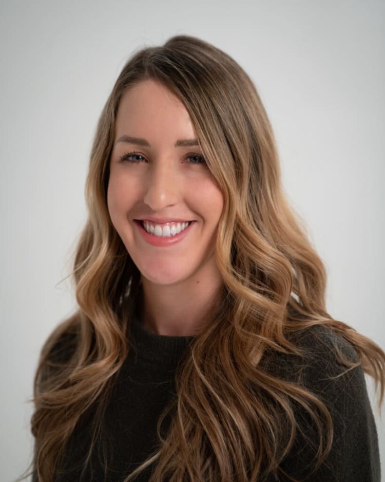 Long wavy light brown hair with blonde highlights styled loose over a dark green knit sweater against a plain light gray background.