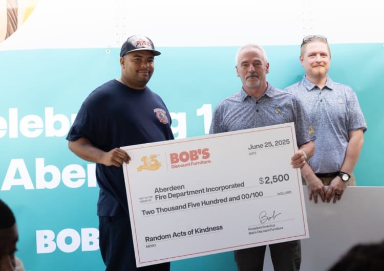 Three men hold a large $2,500 check from Bob's Discount Furniture dated June 25, 2025, awarded to Aberdeen Fire Department Incorporated for Random Acts of Kindness.