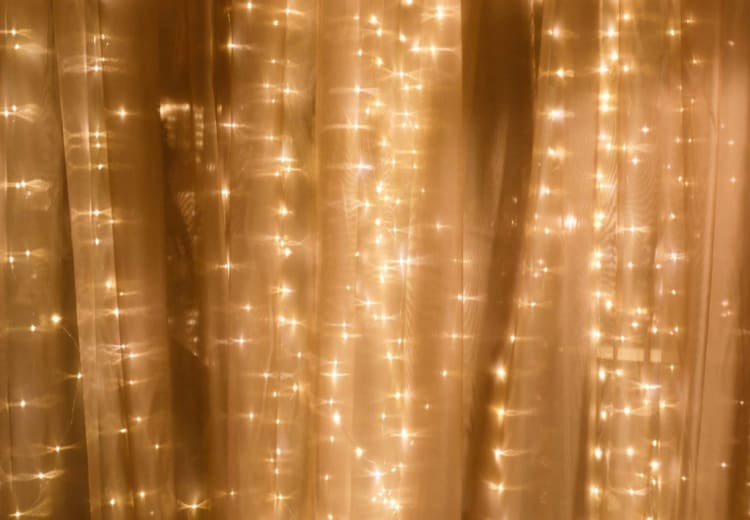Soft warm white fairy lights glowing behind sheer beige curtains, creating a cozy and festive ambient lighting effect.