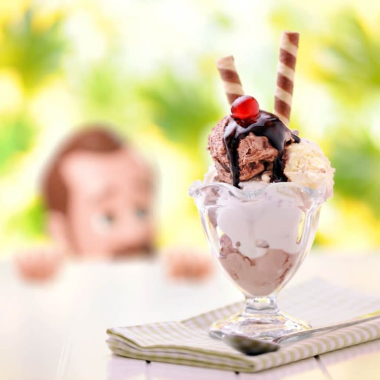 Chocolate and vanilla ice cream scoops in a clear glass dessert cup topped with chocolate syrup, a red cherry, and two striped wafer sticks on a striped napkin.