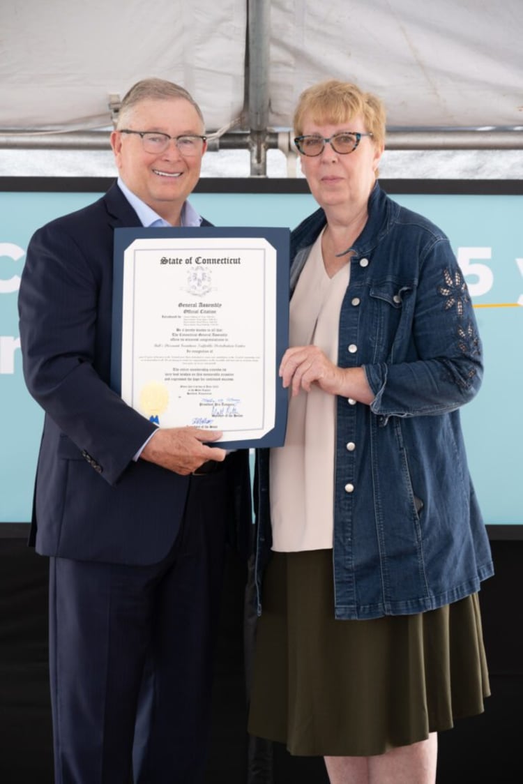 Two people holding a State of Connecticut General Assembly official citation certificate, recognizing the Connecticut School for the Deaf.