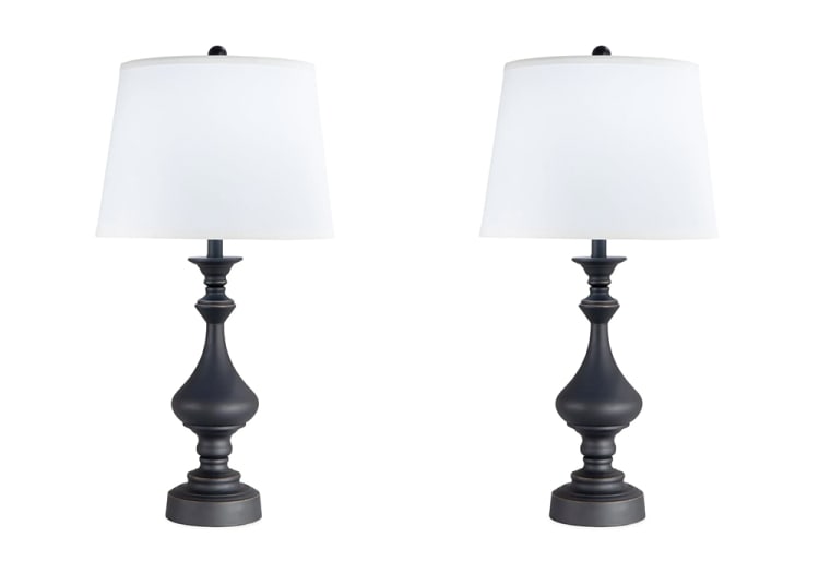 Pair of black metal table lamps with curvy bases and white fabric drum shades, suitable for living room or bedroom lighting.