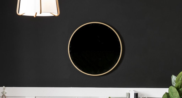 Round wall mirror with a thin wooden frame mounted on a black wall, suitable for modern home decor and interior design.