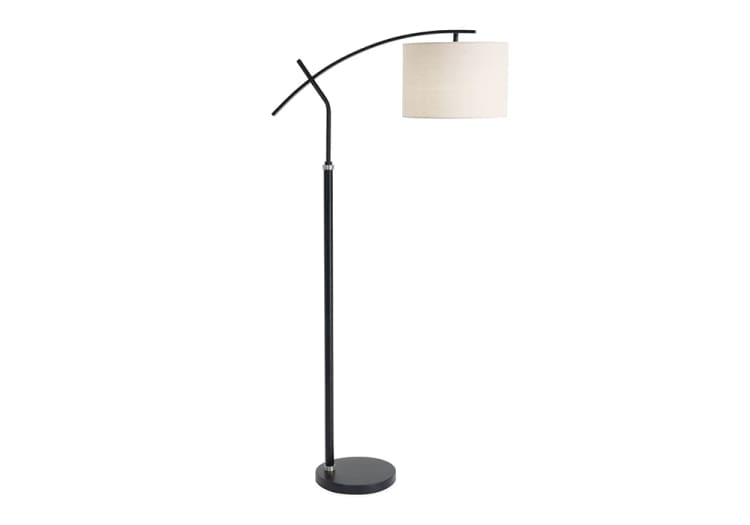 Modern black metal arc floor lamp with a round beige fabric drum shade, adjustable curved arm, and circular base for living room lighting.