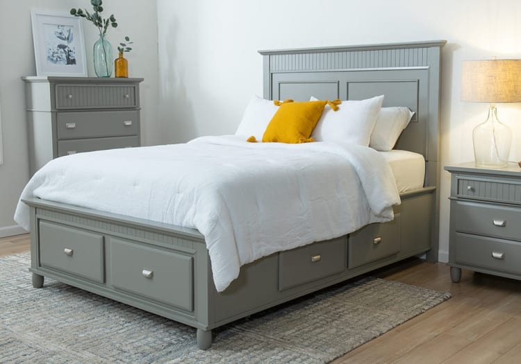 Gray wooden bed frame with white bedding and mustard yellow pillows, featuring built-in storage drawers, matching nightstand and dresser in modern bedroom setting.