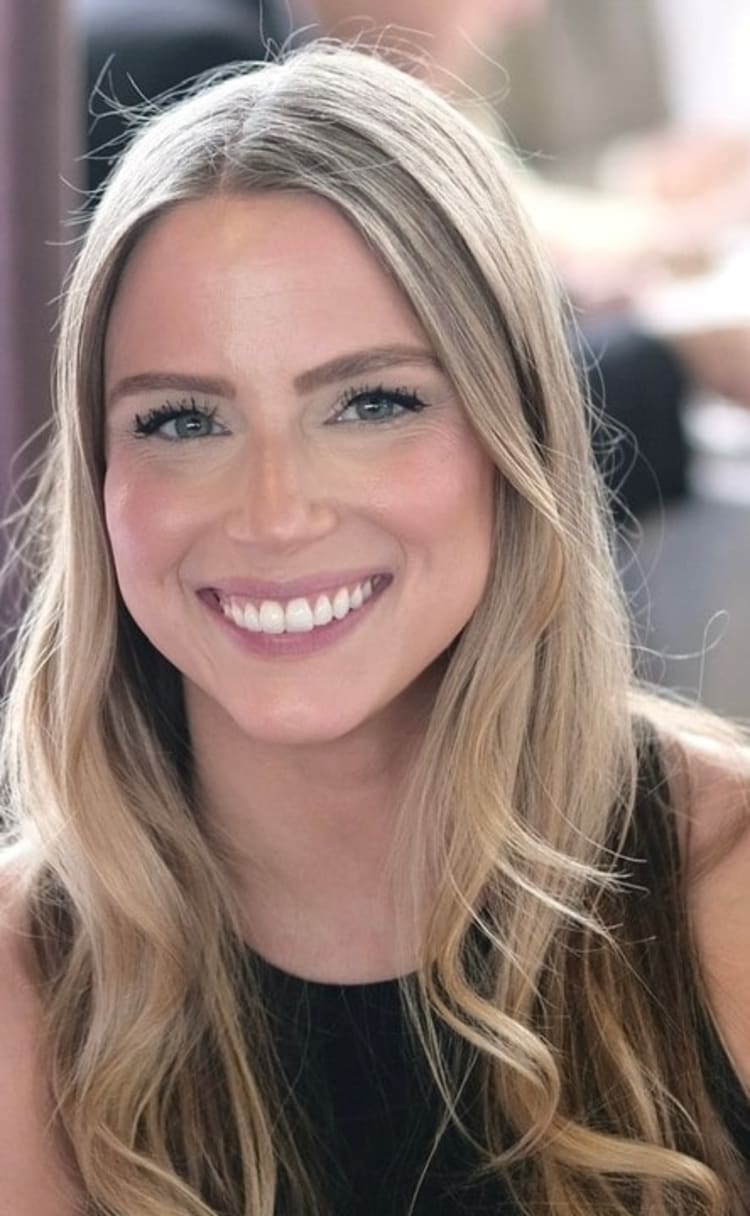 Long, wavy blonde hair with darker roots, styled loosely over shoulders, worn with a sleeveless black top against a blurred background.