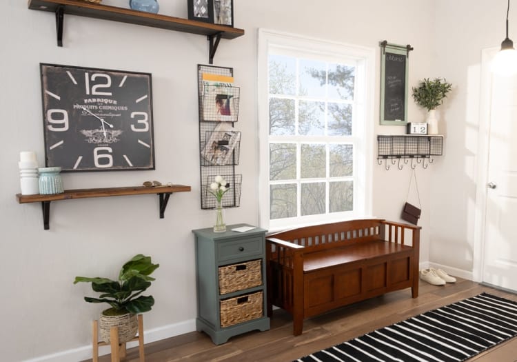 Entryway with a wooden storage bench, gray cabinet with wicker drawers, large black wall clock reading 10:30, wire magazine rack, and black-and-white striped rug.