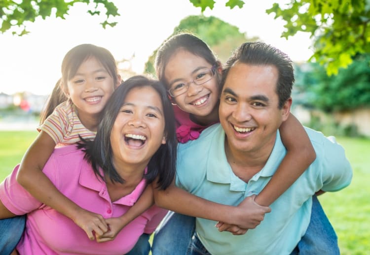 Two children piggybacking on adults outdoors in a green park, showcasing family bonding and playful interaction in casual clothing.