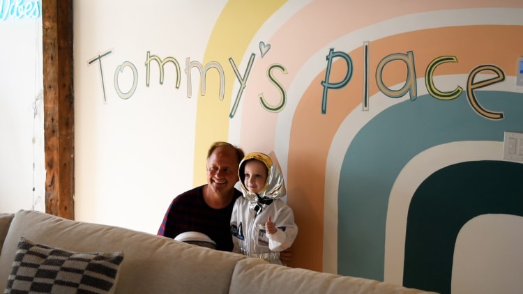 Man and child in astronaut costume giving thumbs up, standing in front of a colorful wall mural with "Tommy's place" text.