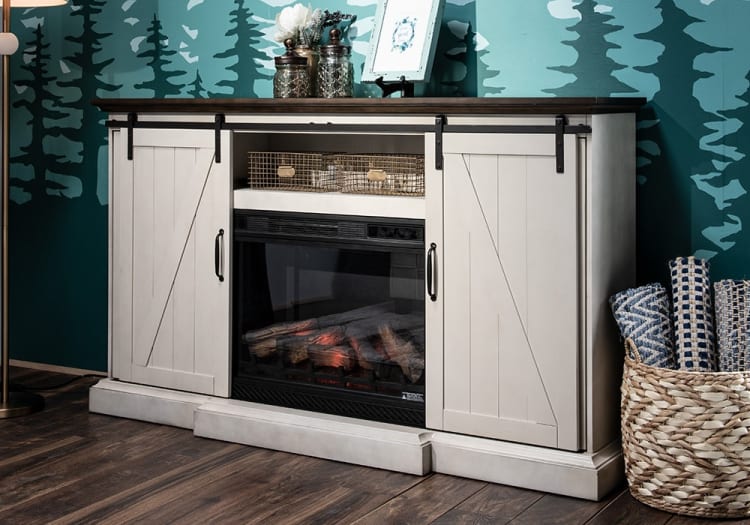 White wooden sliding barn door electric fireplace cabinet with dark wood top, decorative glass jars, and woven basket with blue patterned rugs.