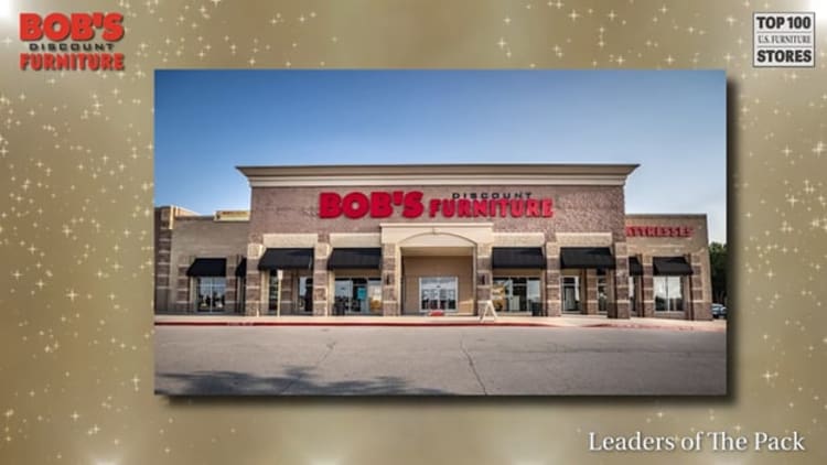 Bob's Discount Furniture storefront with beige brick facade, large red and black signage reading "BOB'S DISCOUNT FURNITURE," black window awnings, and clear blue sky background. Text in image includes "BOB'S DISCOUNT FURNITURE" in top left corner and "TOP 100 U.S. FURNITURE STORES" in top right corner, with "Leaders of The Pack" at bottom right.