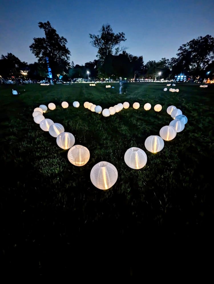 White paper lanterns arranged in a glowing heart shape on grass at night, creating a romantic outdoor light display.