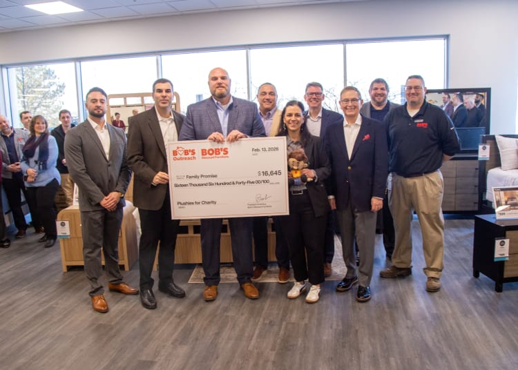 Group of people standing indoors holding a large check from Bob's Discount Furniture and Bob's Outreach dated Feb. 13, 2026, for $16,645 to Family Promise for Plushies for Charity.