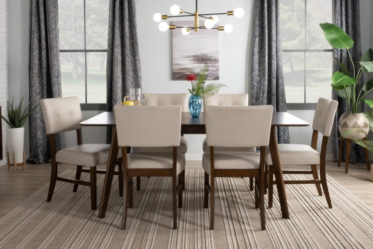 Modern dining room set with six beige upholstered chairs and a dark wood rectangular table on a striped beige rug, featuring large windows and contemporary lighting.