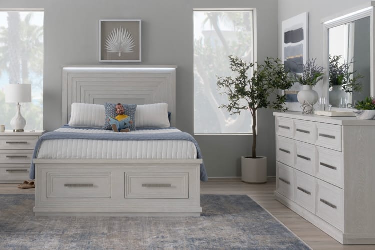 Modern bedroom featuring a light wood platform bed with storage drawers, matching dresser, blue and white bedding, and large windows for natural light.