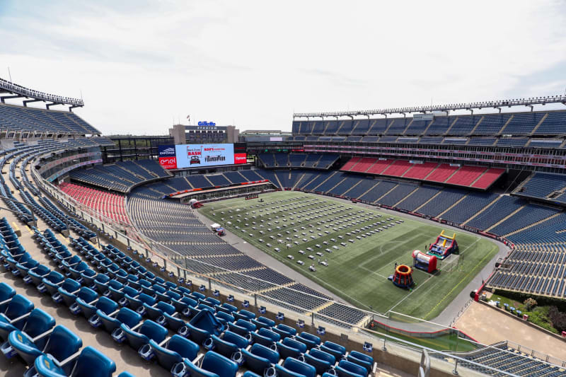 Gillette Stadium with empty blue and red seats, a football field set up with spaced tables, and inflatable play structures for an event.
