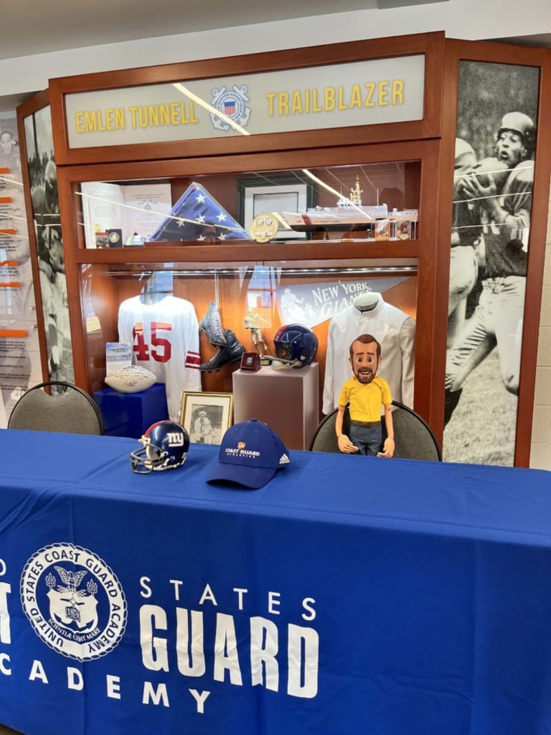 Display case labeled "Emlen Tunnell Trailblazer" featuring a folded American flag, football memorabilia, Coast Guard hat, New York Giants helmet, and a blue tablecloth with "United States Coast Guard Academy" text.