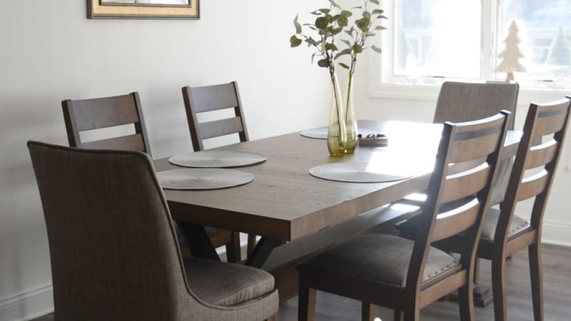 Rectangular wooden dining table with a dark finish, six matching chairs with cushioned seats, and decorative vases with greenery, set in a bright, modern dining room.