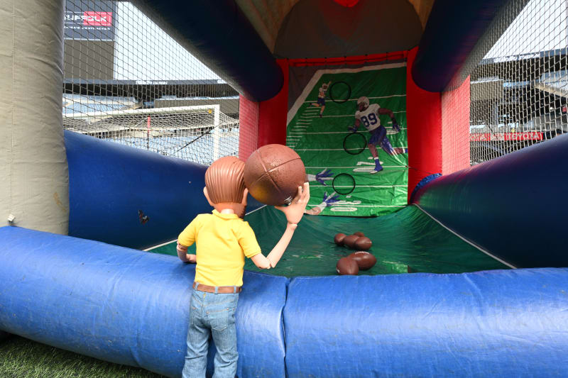 Inflatable football toss game with a cartoon figure holding a football, featuring multiple footballs and target rings on a green field background.