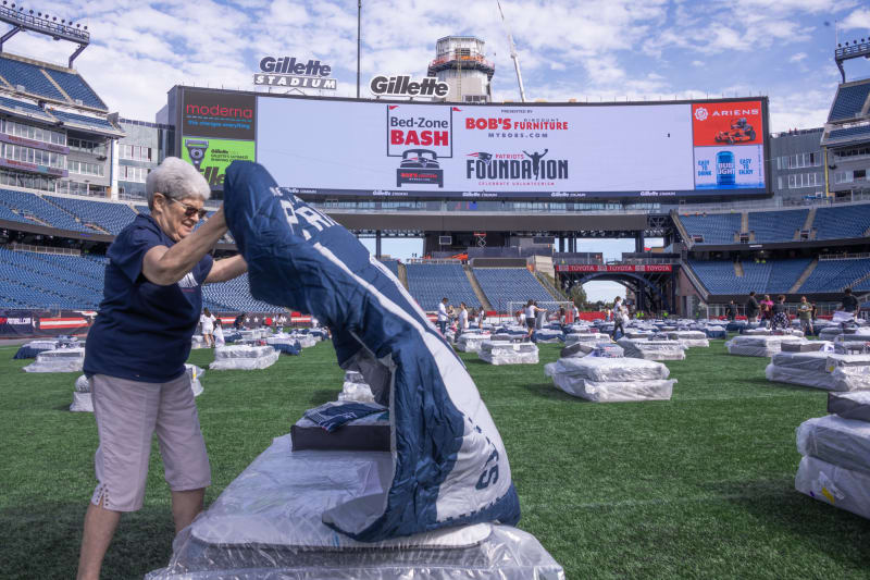 Person setting up a Patriots-themed sleeping bag on a mattress covered in plastic on the field at Gillette Stadium for the Bed-Zone Bash event.