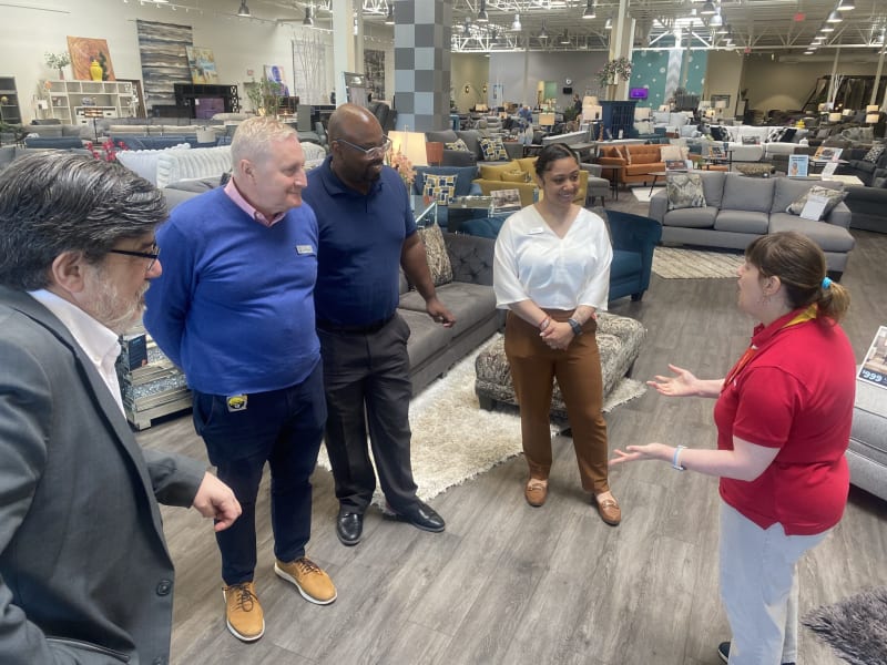 Group of five people standing and conversing inside a modern furniture store, surrounded by various sofas, chairs, and home decor items on display.