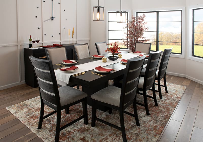 Modern dining room with a dark wood rectangular table, eight cushioned chairs with gray upholstery, a patterned area rug, and large windows providing natural light.