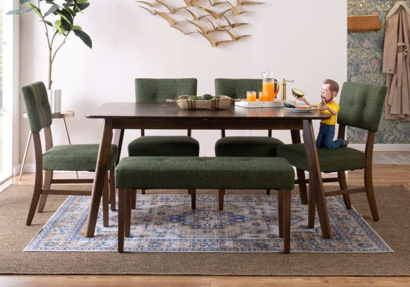 Modern dining room set with dark wood table, green upholstered chairs and bench, decorative wall art, and a tray with orange juice and avocados.