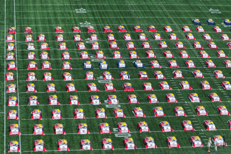 Rows of red and blue racing wheelchairs with yellow helmets arranged in a grid on a green sports field, likely for a race event.