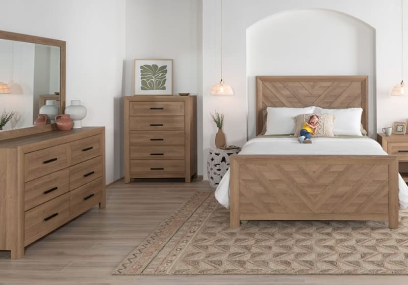 Modern bedroom with natural wood furniture including a queen bed with chevron headboard, matching dresser, chest of drawers, and nightstand on patterned rug.